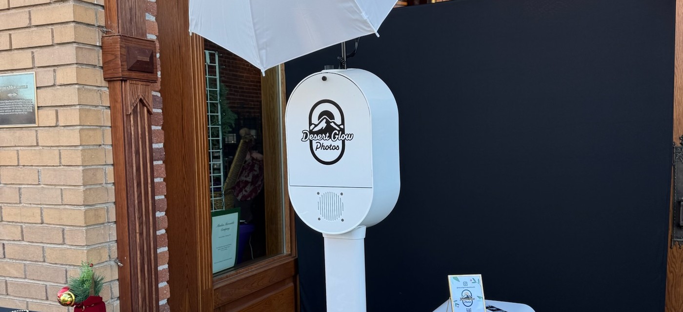 White photo booth with the Desert Glow Photos logo under an umbrella light beside a black backdrop