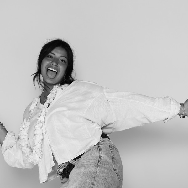 Black-and-white shot of a woman in a white shirt and flower lei posing with arms outstretched, tongue out